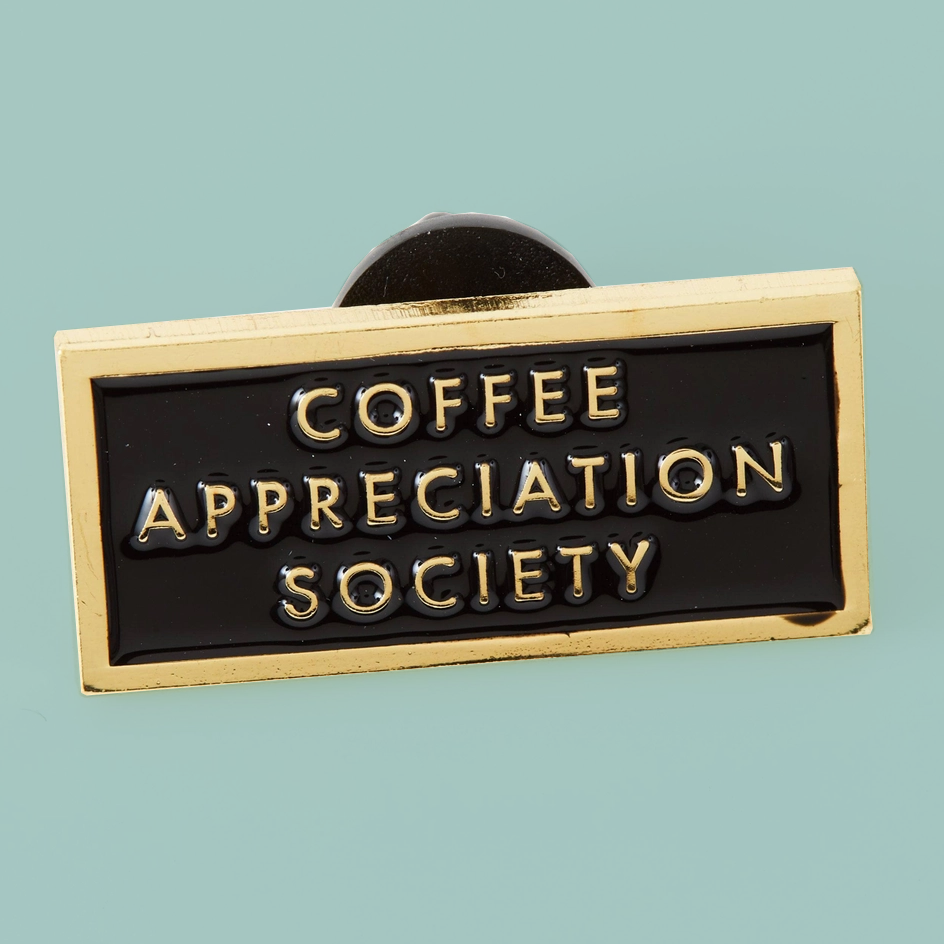 A rectangular enamel pin with a gold border and black face, featuring the words 'COFFEE APPRECIATION SOCIETY' in raised gold lettering, shown on a solid light blue background.