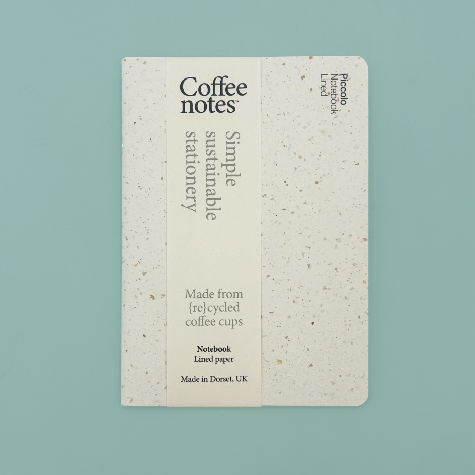 A Coffee Notes simple sustainable notebook made from recycled coffee cups, shown closed with its paper sleeve on a solid teal background.