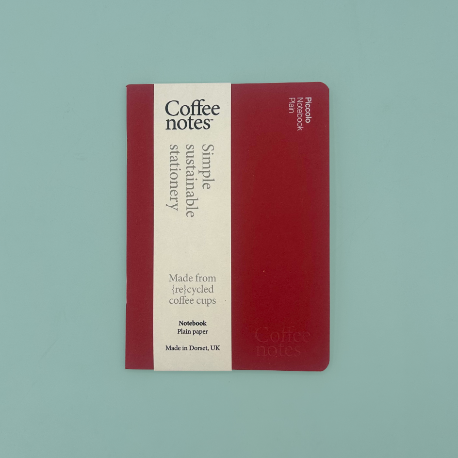 A Coffee Notes stationery notebook with a deep red cover and a cream-colored vertical label, photographed flat on a solid light teal background.