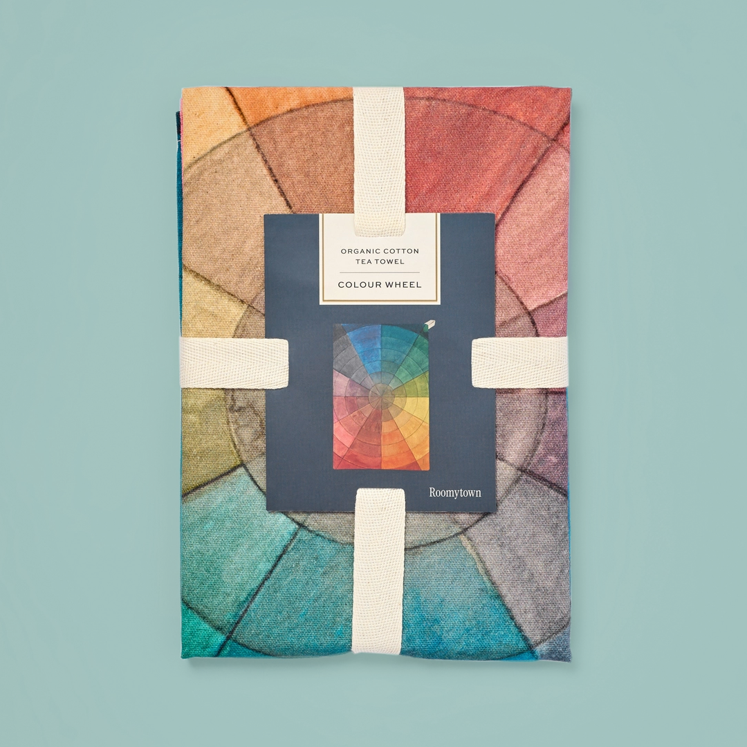 Packaged tea towel with a colour wheel pattern in watercolour, on a blue background.