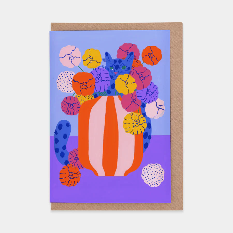 A portrait orientation greetings card with a  blue and purple background with a digital illustration of a blue spotted cat inside an orange and pink striped vase with orange, yellow, pink, and purple flowers. The card is on a brown envelope on a plain backdrop. 