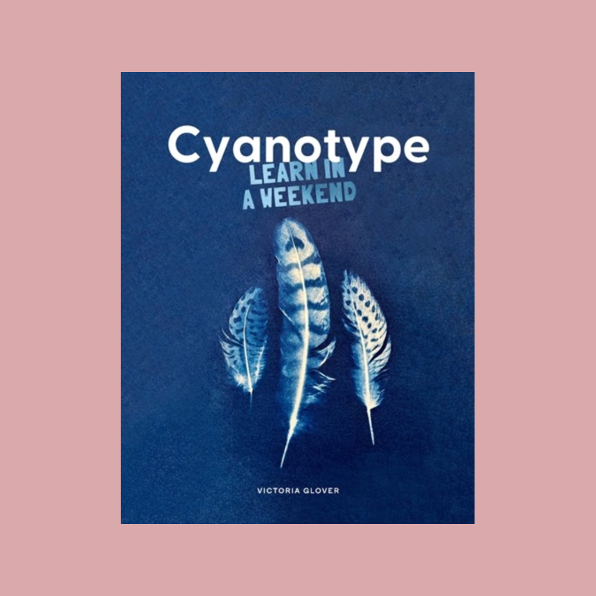 Book cover for 'Cyanotype: Learn in a Weekend' by Victoria Clover, featuring a dark blue background with three white and light blue feathers and white title text, centered on a dusty pink background.