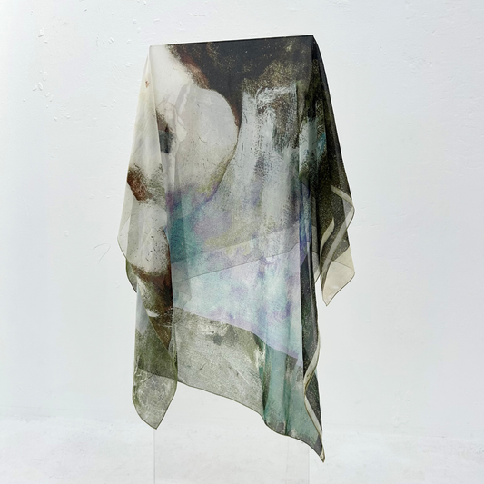 Grey, blue, and green silk scarf draped over a clear stand. 