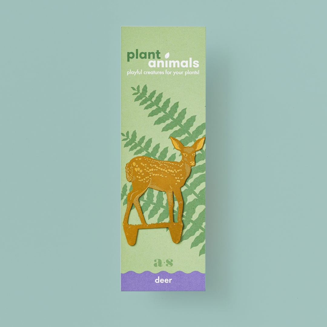 Deer-shaped brass decoration, with points for planting in soil, on a green and purple backing card. 