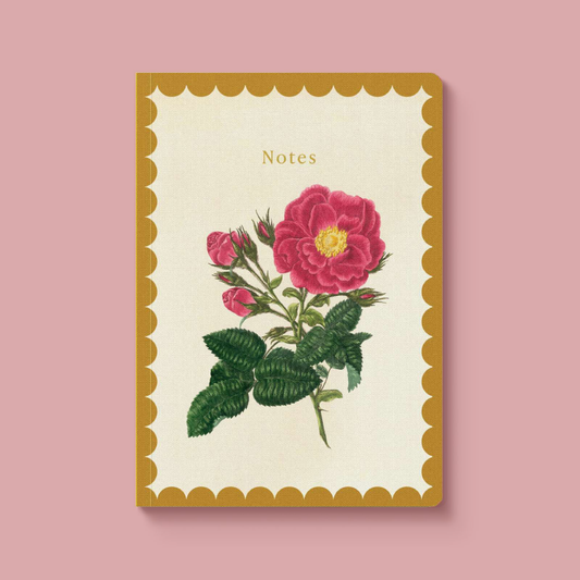 A cream-colored notebook with a scalloped mustard yellow border, featuring a vintage-style illustration of pink roses and green leaves on the cover, with the word 'Notes' printed at the top. The notebook is centered against a solid dusty pink background.