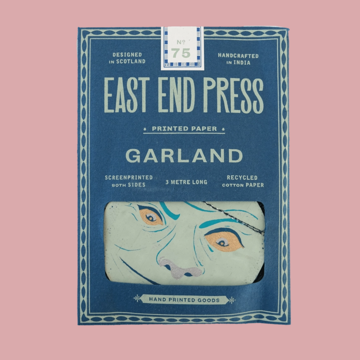 East End Press Garland No. 75 printed paper package, featuring a blue box with a window showing a hand-painted face illustration, set against a solid pink background.