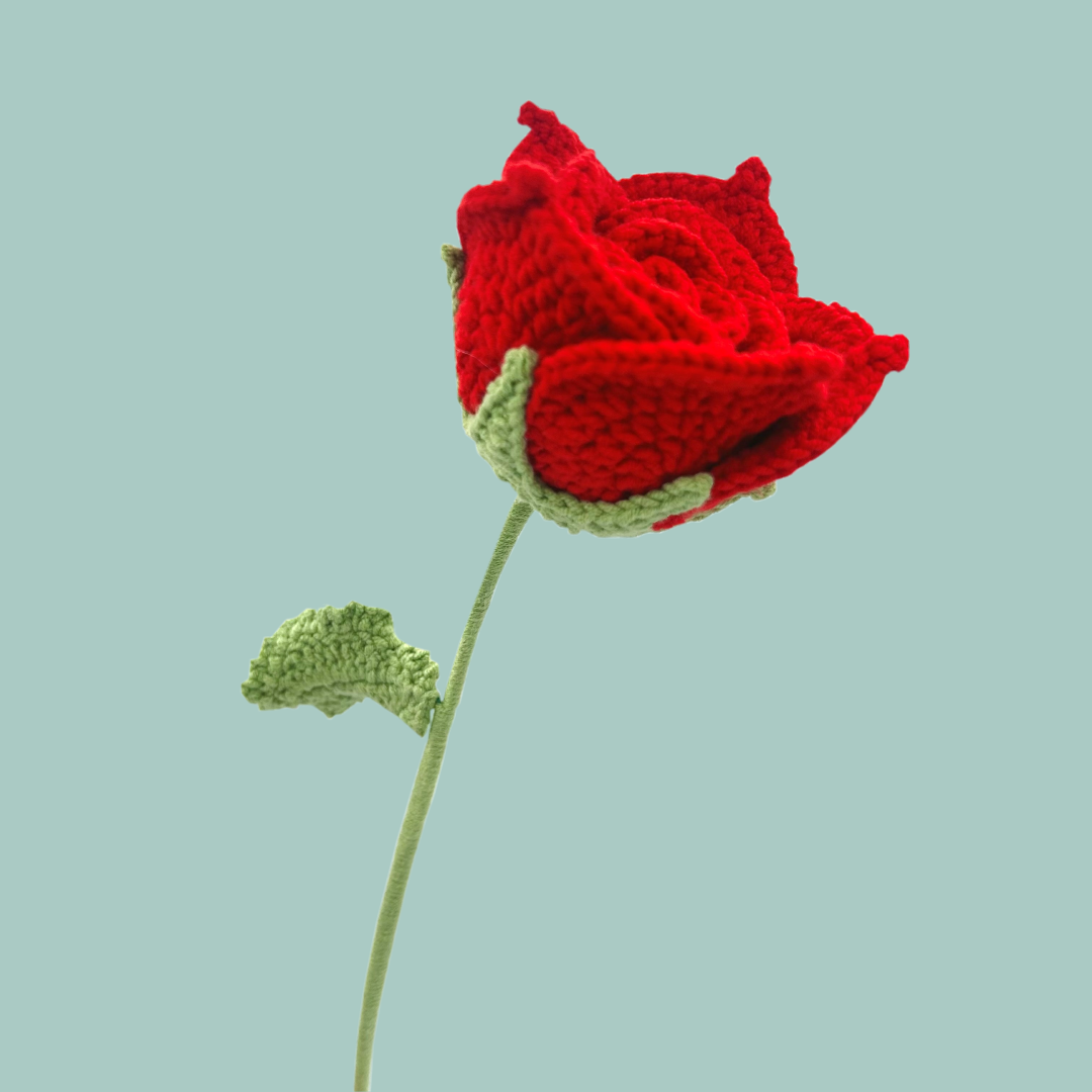Red crochet rose with a green stem on a plain blue background. 
