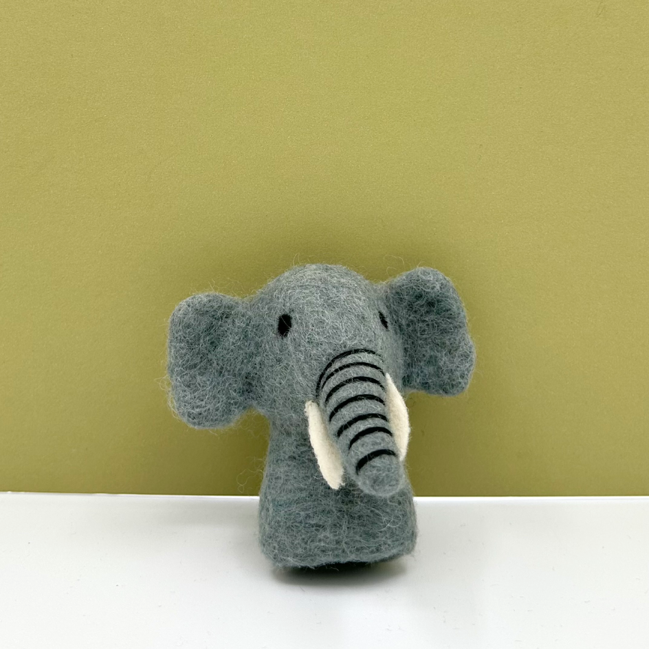 A small felt elephant finger puppet in soft grey with black-and-white striped trunk and white tusks, standing on a white surface against an olive-green background.