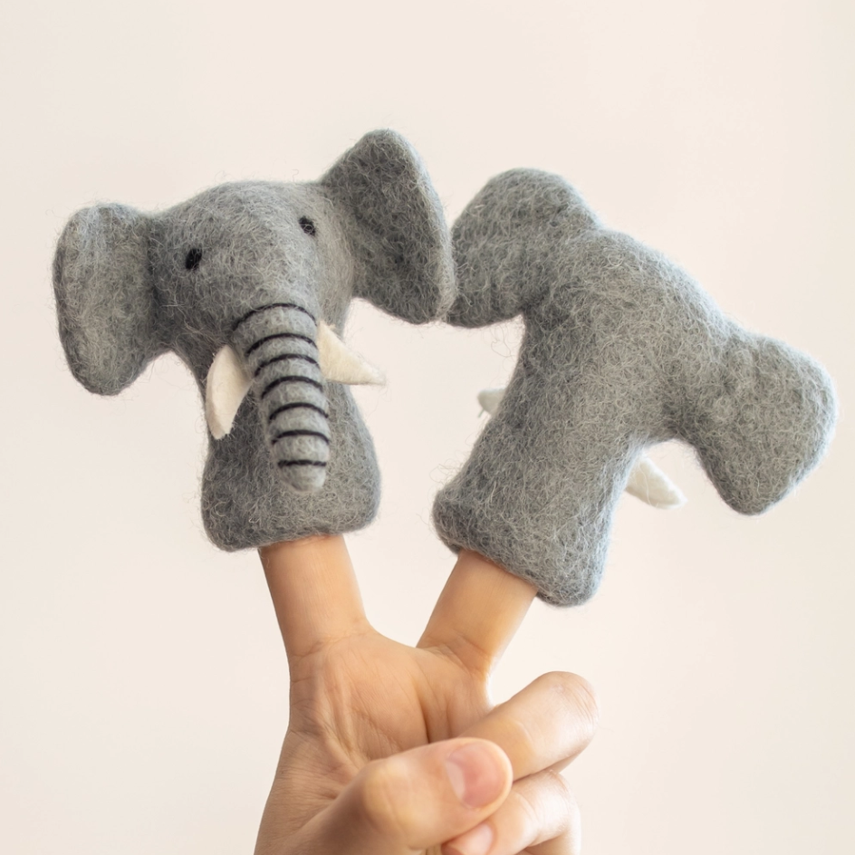 A hand holding two grey felt elephant finger puppets against a plain light beige background.