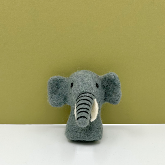A small grey felt elephant finger puppet with black and white stripes on its trunk and a white inner ear, standing on a white surface against a muted olive-green background.