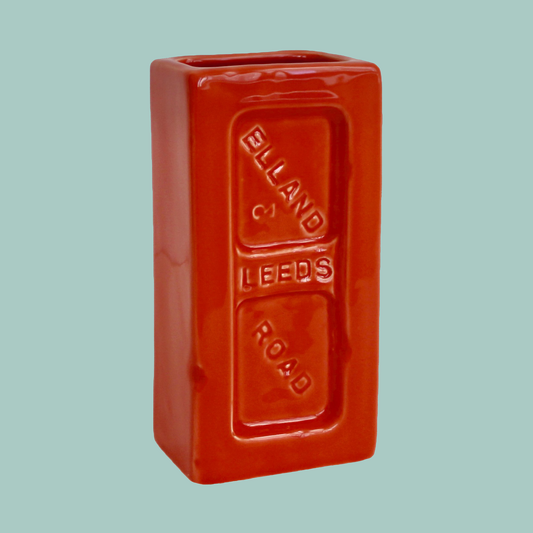 An orange ceramic brick-shaped vase with 'Leeds Elland Road' embossed on the side.