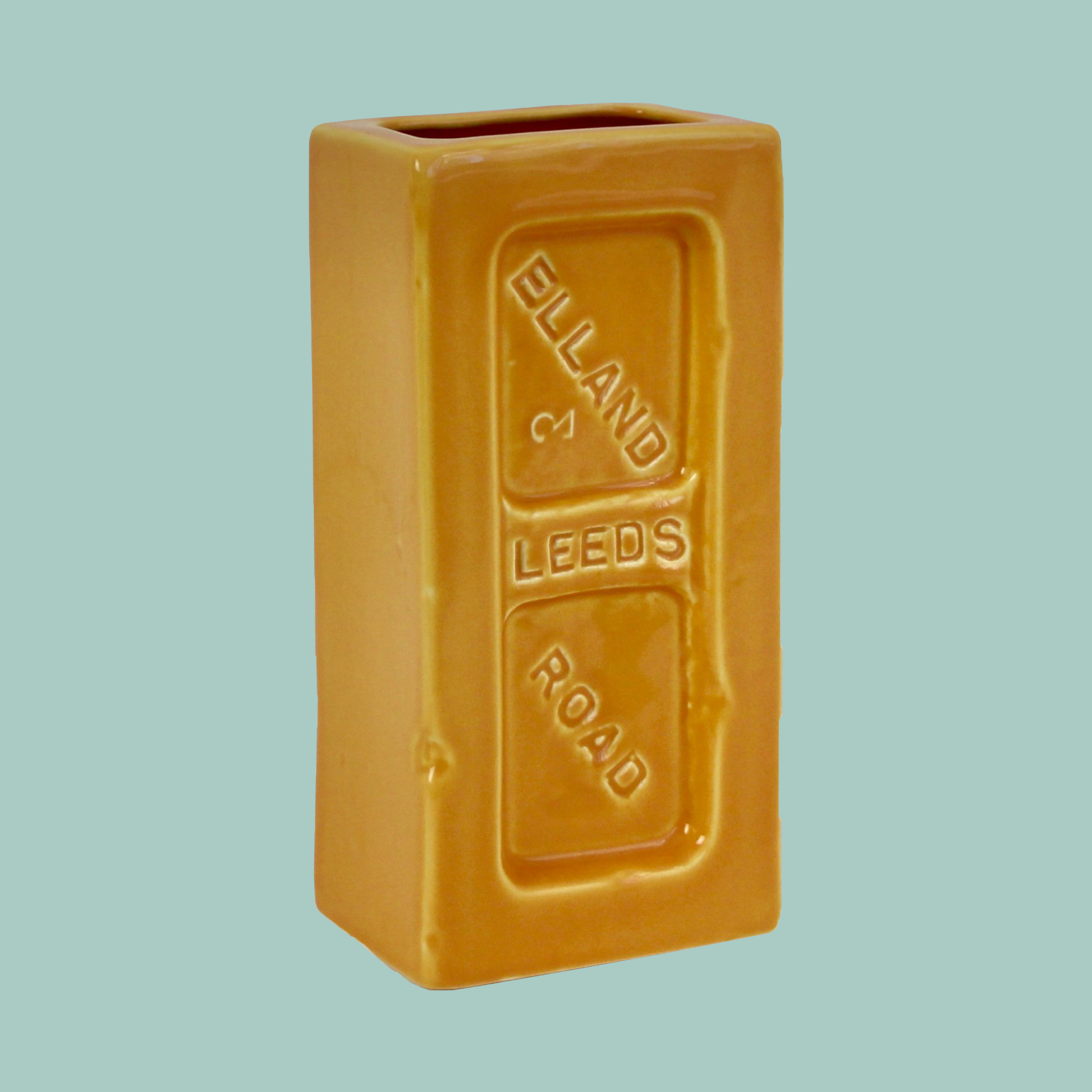 A yellow ceramic brick-shaped vase with 'Leeds Elland Road' embossed on the side.