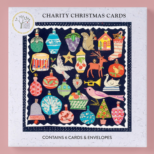 Charity Christmas Cards kit by Canns  Down Press, featuring a white speckled box with a colourful illustration of various Christmas ornaments, stockings, a reindeer, a bird, and other festive motifs on a dark navy background. The box is set against a solid pink background.