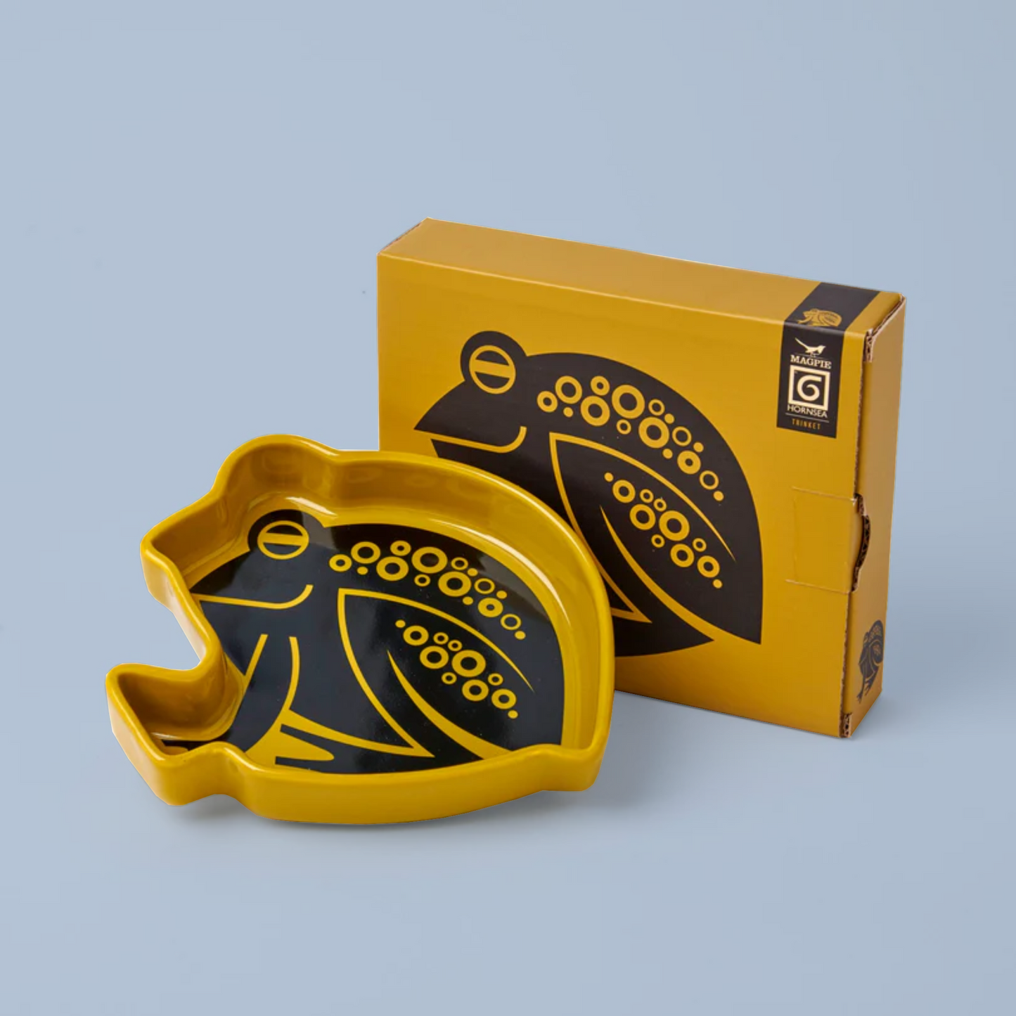 Yellow and black decorative dish with matching packaging on a light blue background