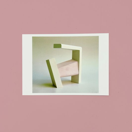 Modern sculpture of a geometric design on a white postcard. The postcard is on a pink background.