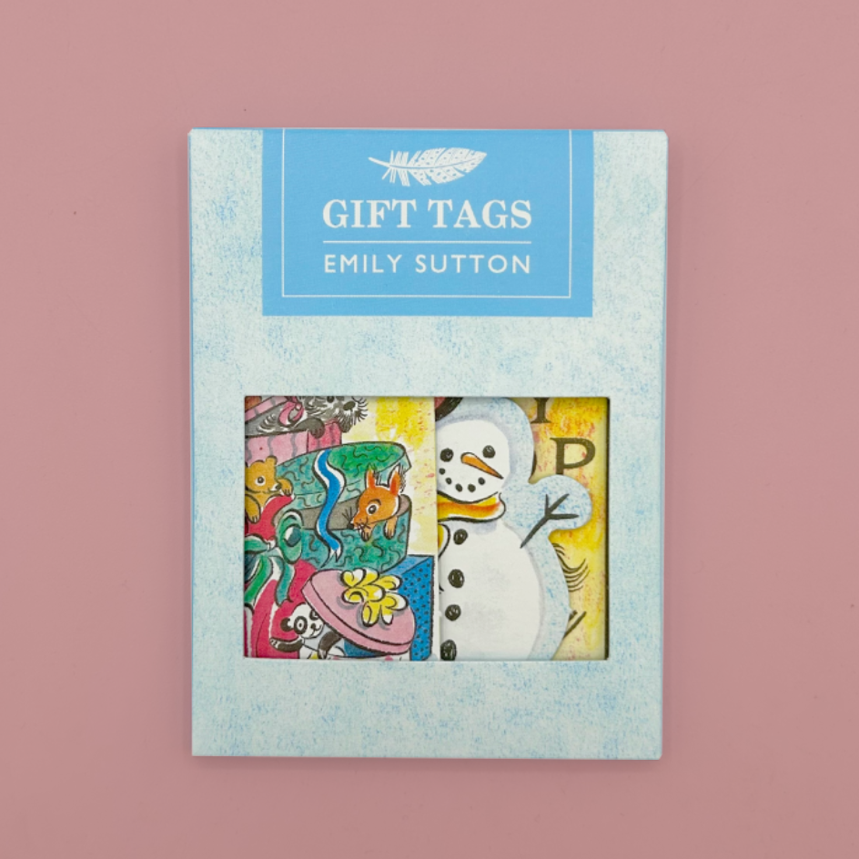 A package of Emily Sutton Gift Tags on a dusty pink background. The light blue textured box features a window showing two colorful illustrated tags: one with a snowman and the other with  a stack of boxes with toys inside.