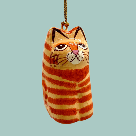 A cat shaped ornament painted in light and dark orange stripes, hanging from a gold string on a blue background. 