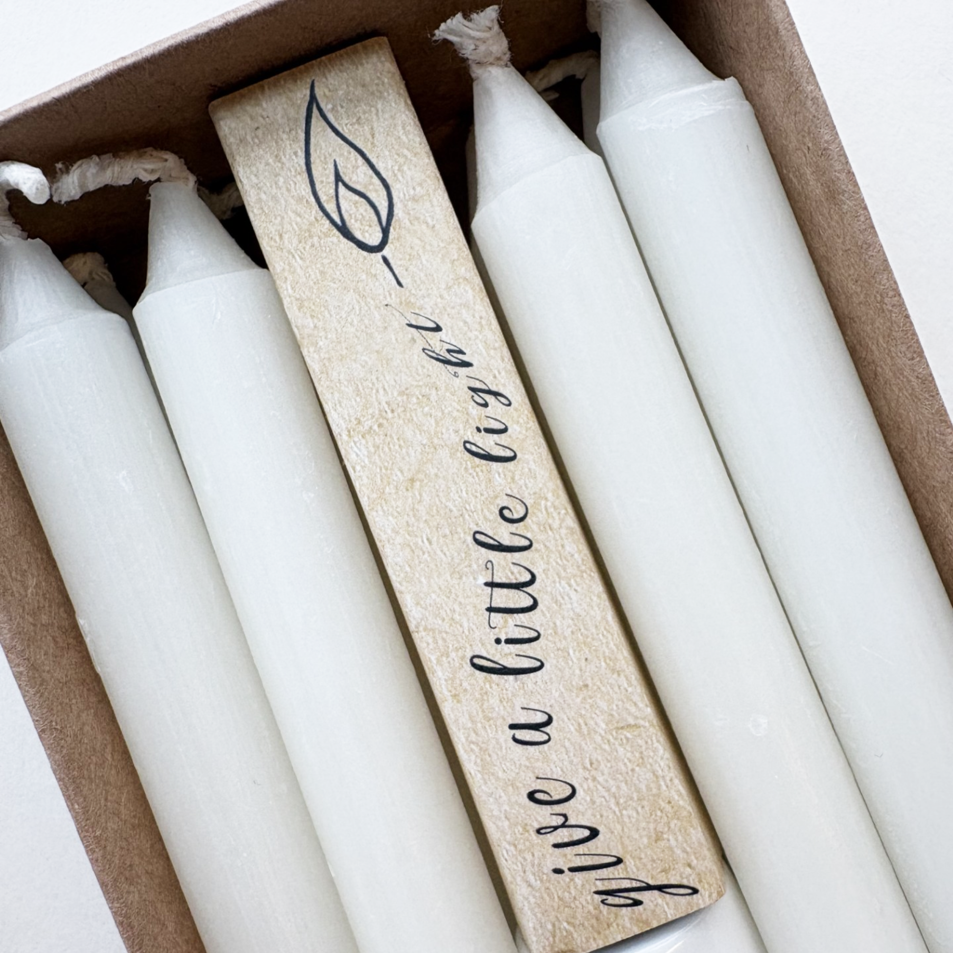 Close up of candles and 'give a little light' slogan on packaging.