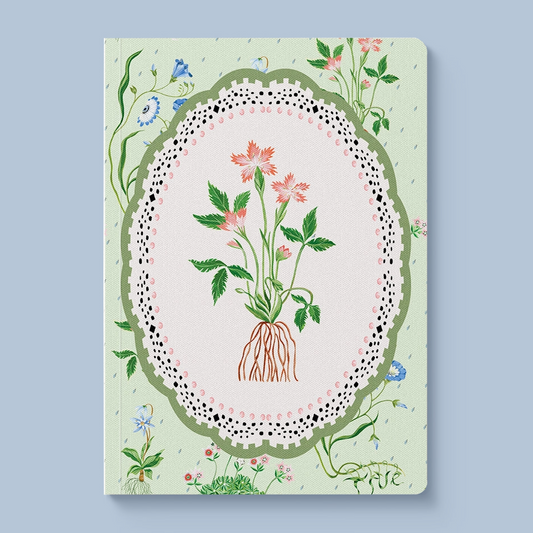 A hardcover notebook with a light green cover decorated with a central botanical illustration of pink flowers and green leaves inside an oval frame with a lace-like border, set against a solid light blue background.