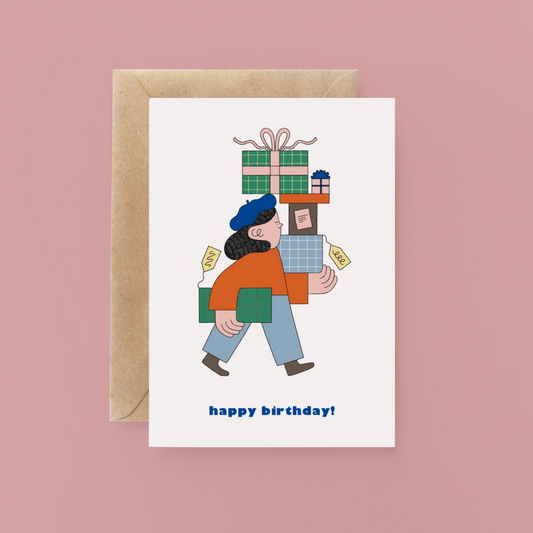 Birthday card with illustration of person carrying gifts and 'happy birthday!' text, on a pink background.