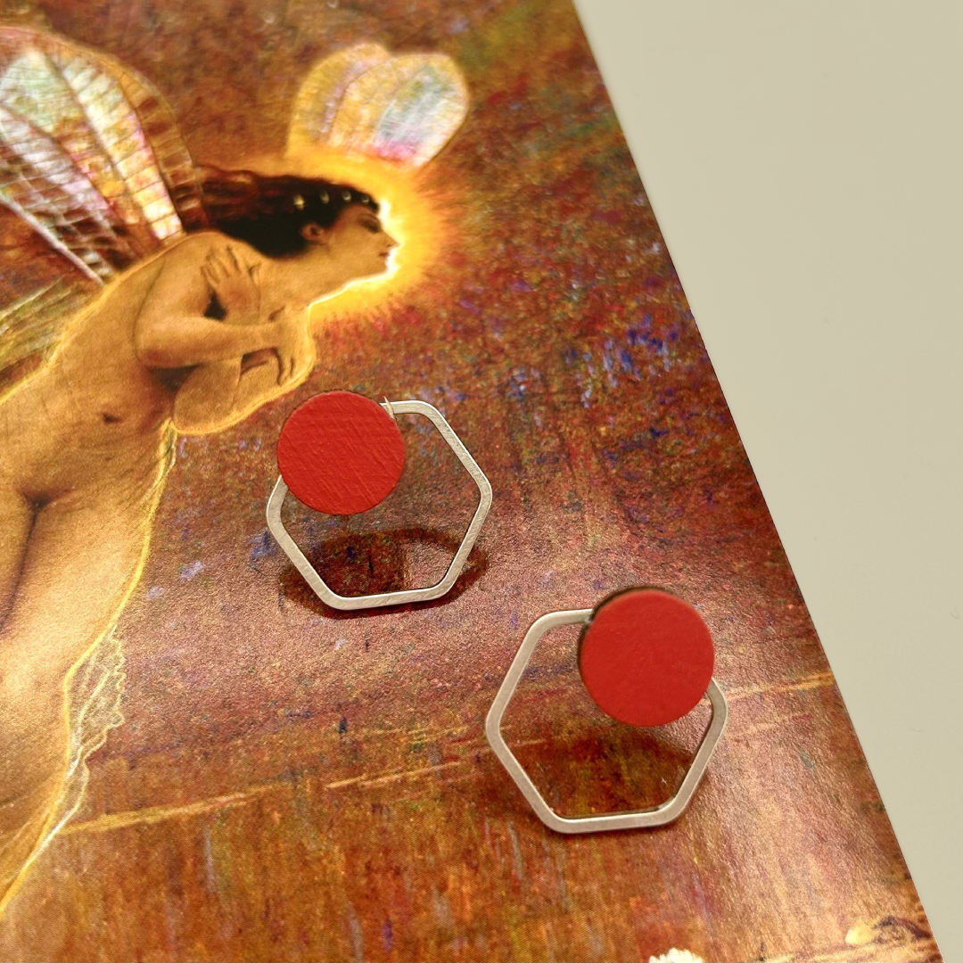 Red earrings with hexagonal frames on a textured surface with artistic background
