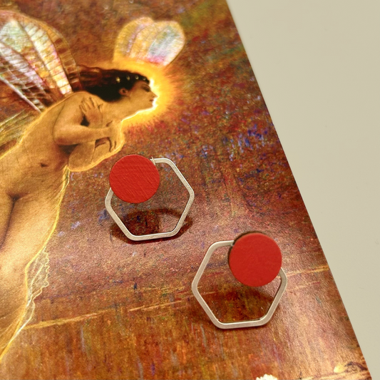 Red earrings with hexagonal frames on a textured surface with artistic background
