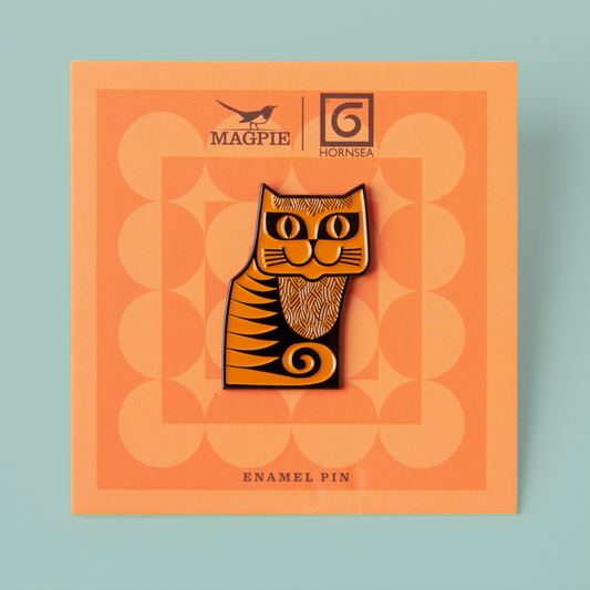 An enamel pin design of an orange cat, on an orange branded backing card. 
