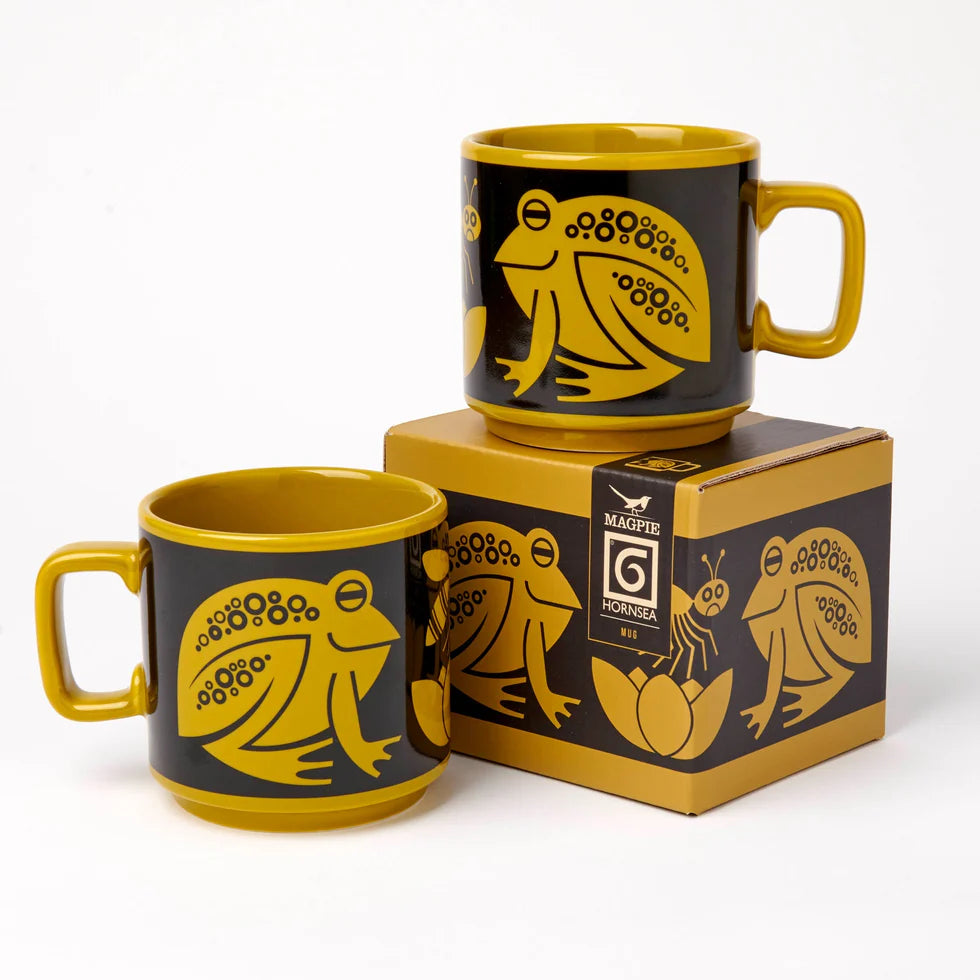 Two black mugs with yellow frog designs on a matching box against a white background