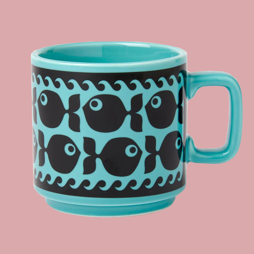 A turquoise ceramic mug with a black band featuring a repeating fish pattern, set against a solid pink background.
