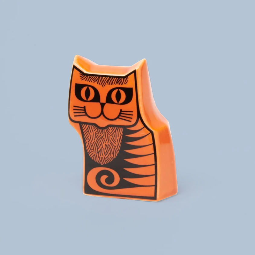 An orange ceramic cat-shaped ornament with black line-art details, set against a solid light blue background.
