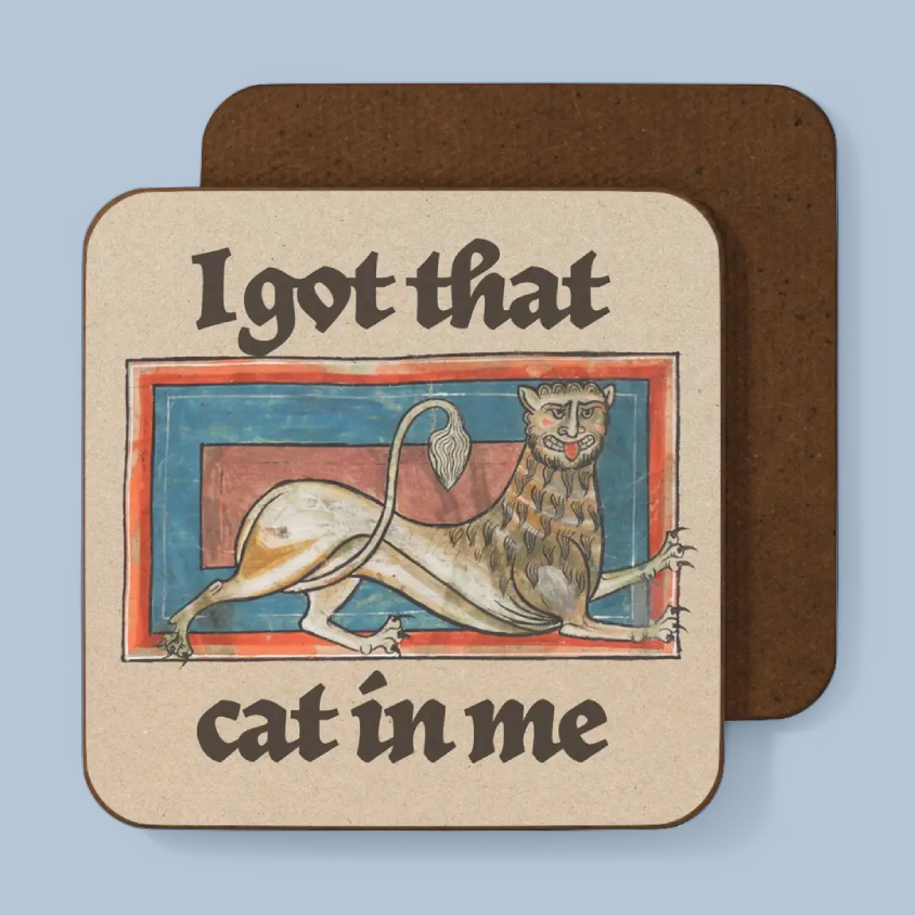 A square coaster with rounded corners shown on a light blue background. The front of the coaster has a beige printed design with the text 'I got that cat in me' and an illustration of a stylized cat in a medieval-style frame.