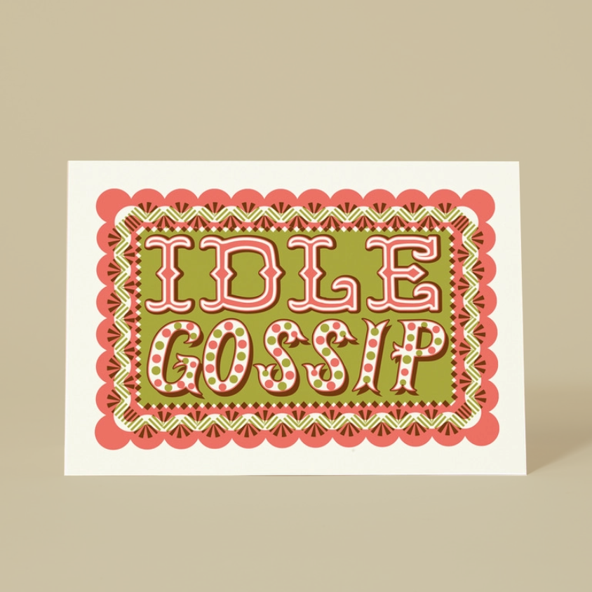 A square greeting card with a retro-style graphic design featuring the words 'IDLE GOSSIP' in pink and white retro lettering on an olive green background, surrounded by a scalloped pink and green border. The card is displayed standing upright on a solid beige background.