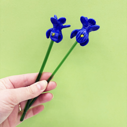 Hand holding two blue flower-shaped objects against a green background