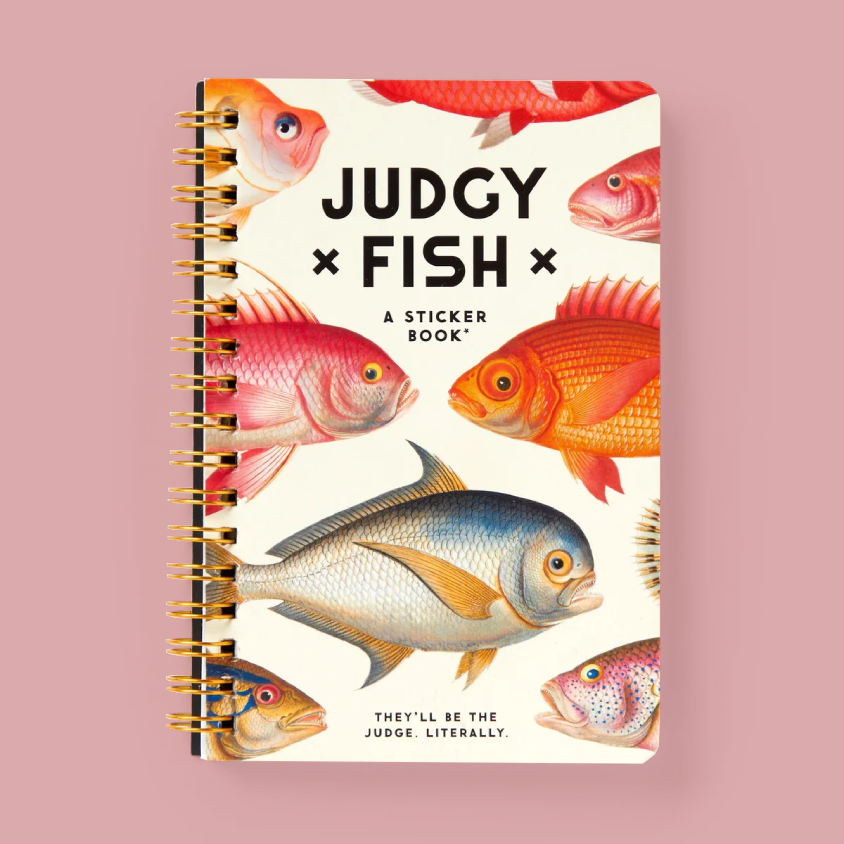 A spiral-bound sticker book titled 'JUDGY FISH' with colorful fish illustrations on the cover, photographed against a solid pink background.