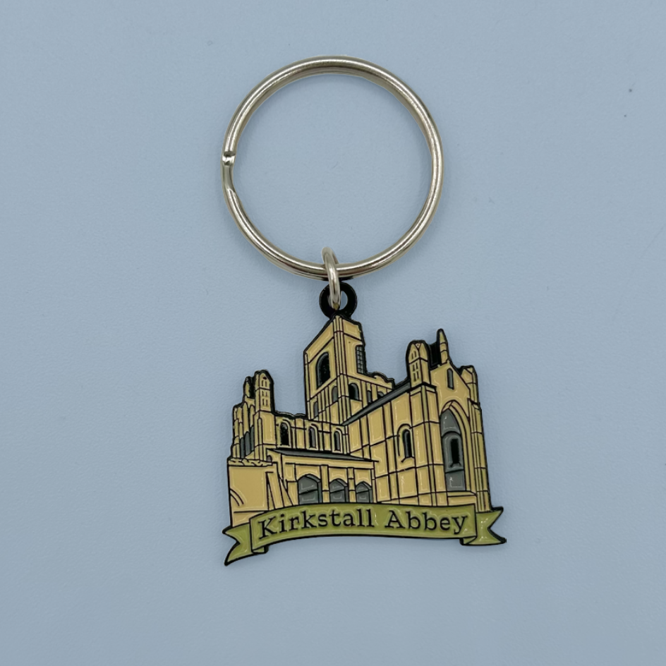 A metal keychain featuring an illustration of Kirkstall Abbey with a banner reading 'Kirkstall Abbey' on a light blue background.