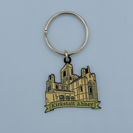 A metal keychain featuring an illustration of Kirkstall Abbey with a banner reading 'Kirkstall Abbey' on a light blue background.