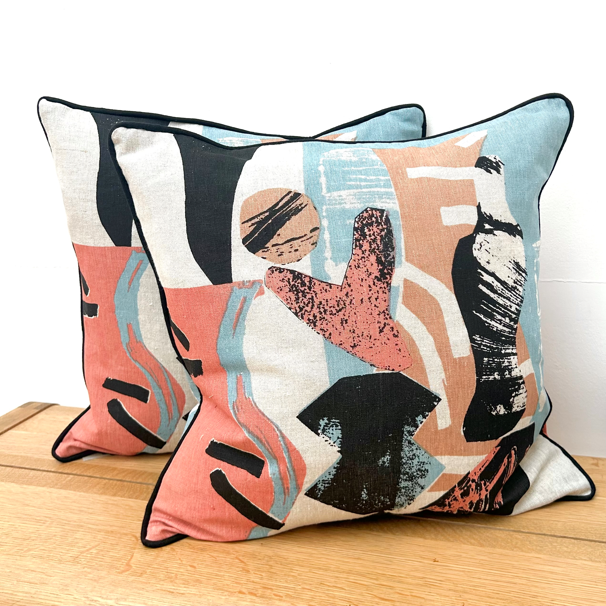 Two abstract patterned pillows on a wooden surface with a white background