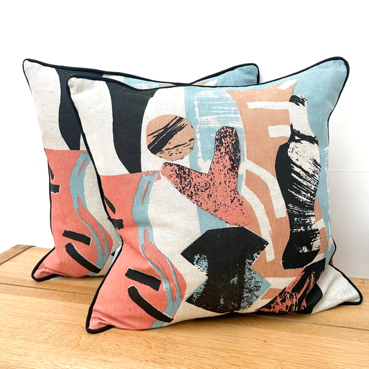 Two abstract patterned pillows on a wooden surface with a white background