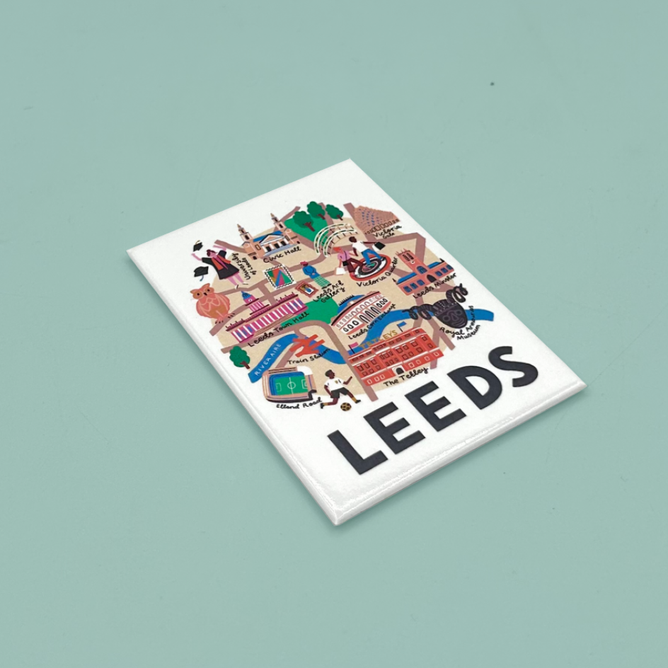 A white rectangular magnet featuring a colorful illustrated map-style graphic with the word "LEEDS" in large black letters, photographed on a muted light blue background.