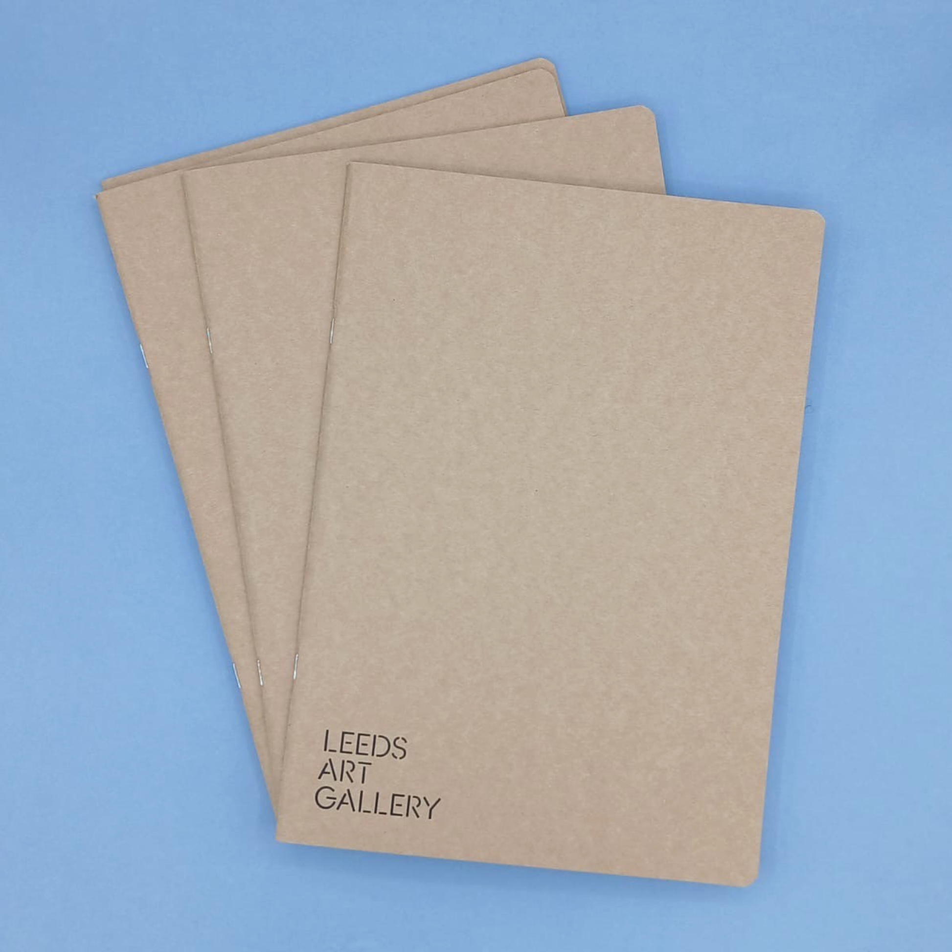 Three brown notebooks with 'Leeds Art Gallery' text on a blue background