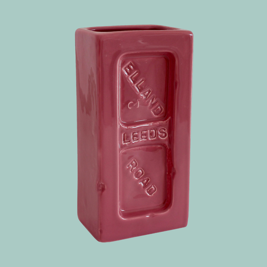 A pink ceramic brick-shaped vase with 'Leeds Elland Road' embossed on the side.