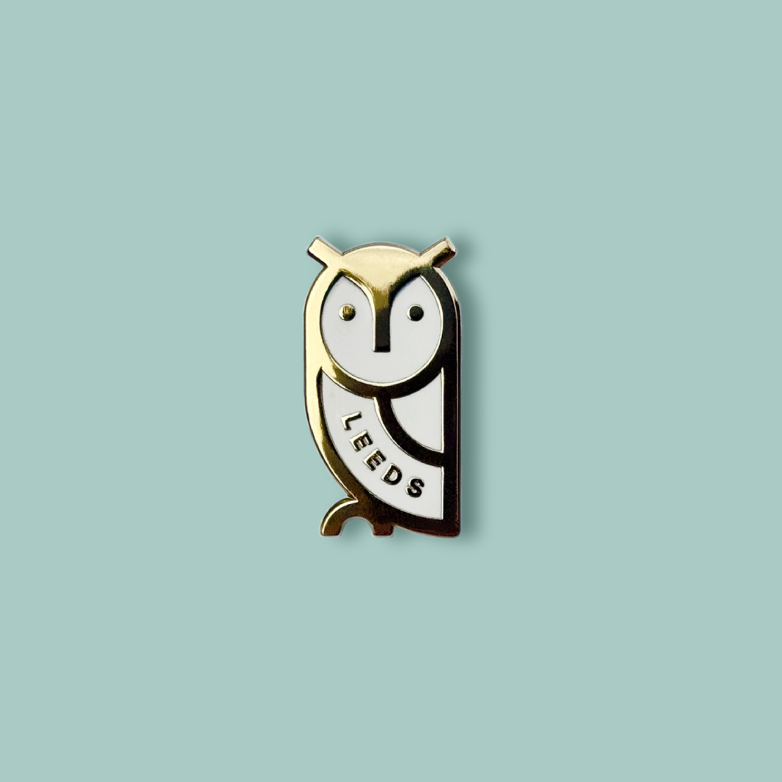 Gold and white owl shaped pin badge on a blue background.