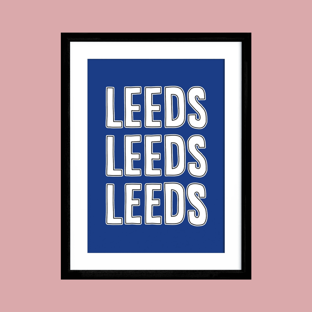 A framed typographic wall art print featuring the word 'LEEDS' repeated three times in large white varsity-style letters on a blue background, shown against a muted pink background.