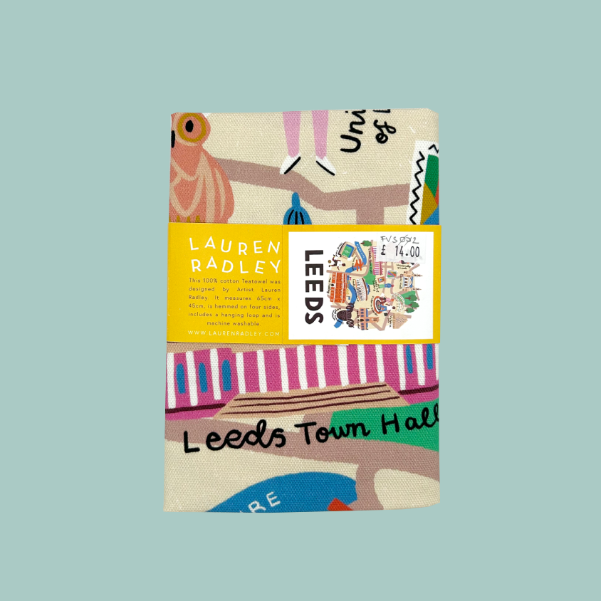 A tea towel featuring a colourful illustrated map design with the text 'Leeds Town Hall' and a yellow label reading 'LAUREN RADLEY' and 'LEEDS'. The product is centered on a solid light blue background.