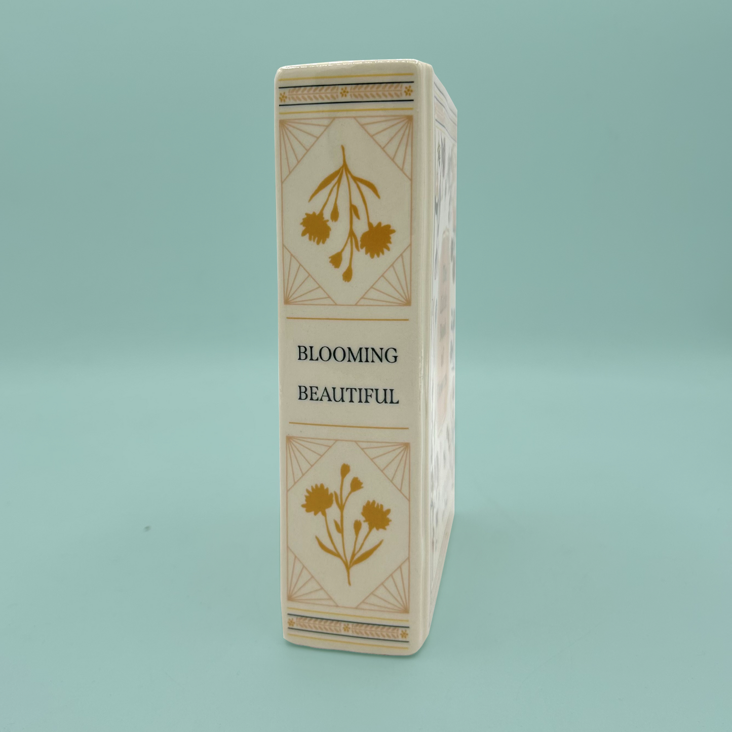 Side of a rectangular vase with floral designs and 'Blooming Beautiful' text on a light blue background