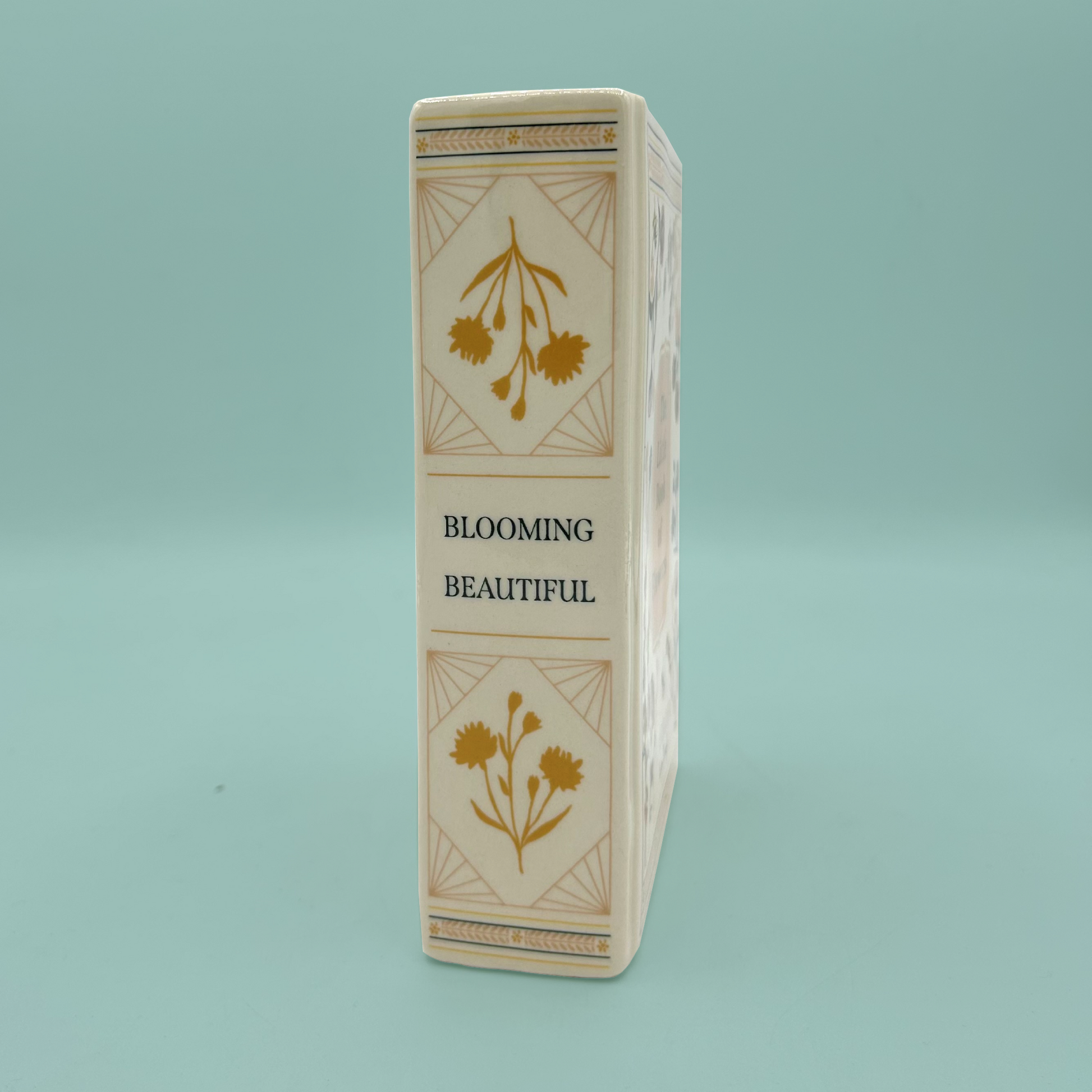 Side of a rectangular vase with floral designs and 'Blooming Beautiful' text on a light blue background