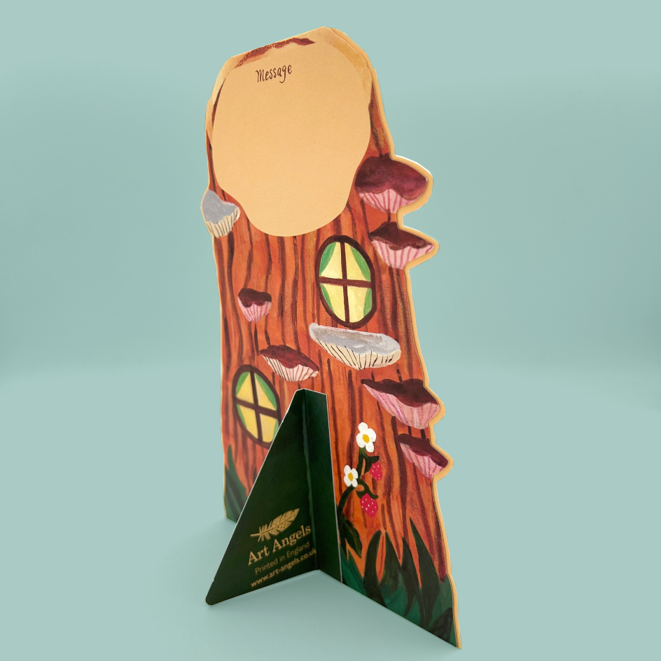 A decorative greetings card shaped like a tree trunk with mushroom shelves, circular window cutouts, small flowers, and a triangular base printed with 'Art Angels' and 'The Art of Living'.