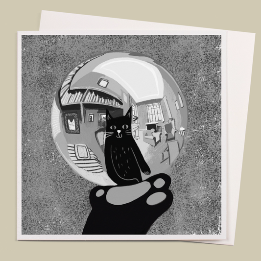 Greyscale greetings card with a cat paw holding a reflecting sphere, showing the reflection of the cat. The card is on a white envelope, on a beige background.
