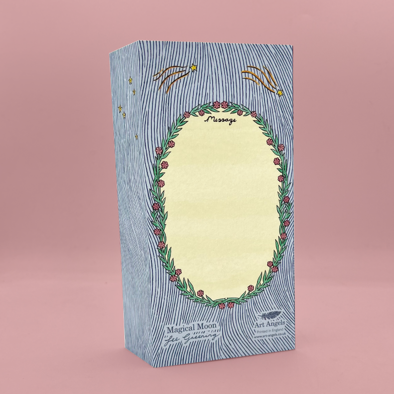 A rectangular greetings card stood upright on a soft pink studio background. The card has a blue-gray striped pattern, a central cream oval window, and a green leafy wreath with red berries around the window.