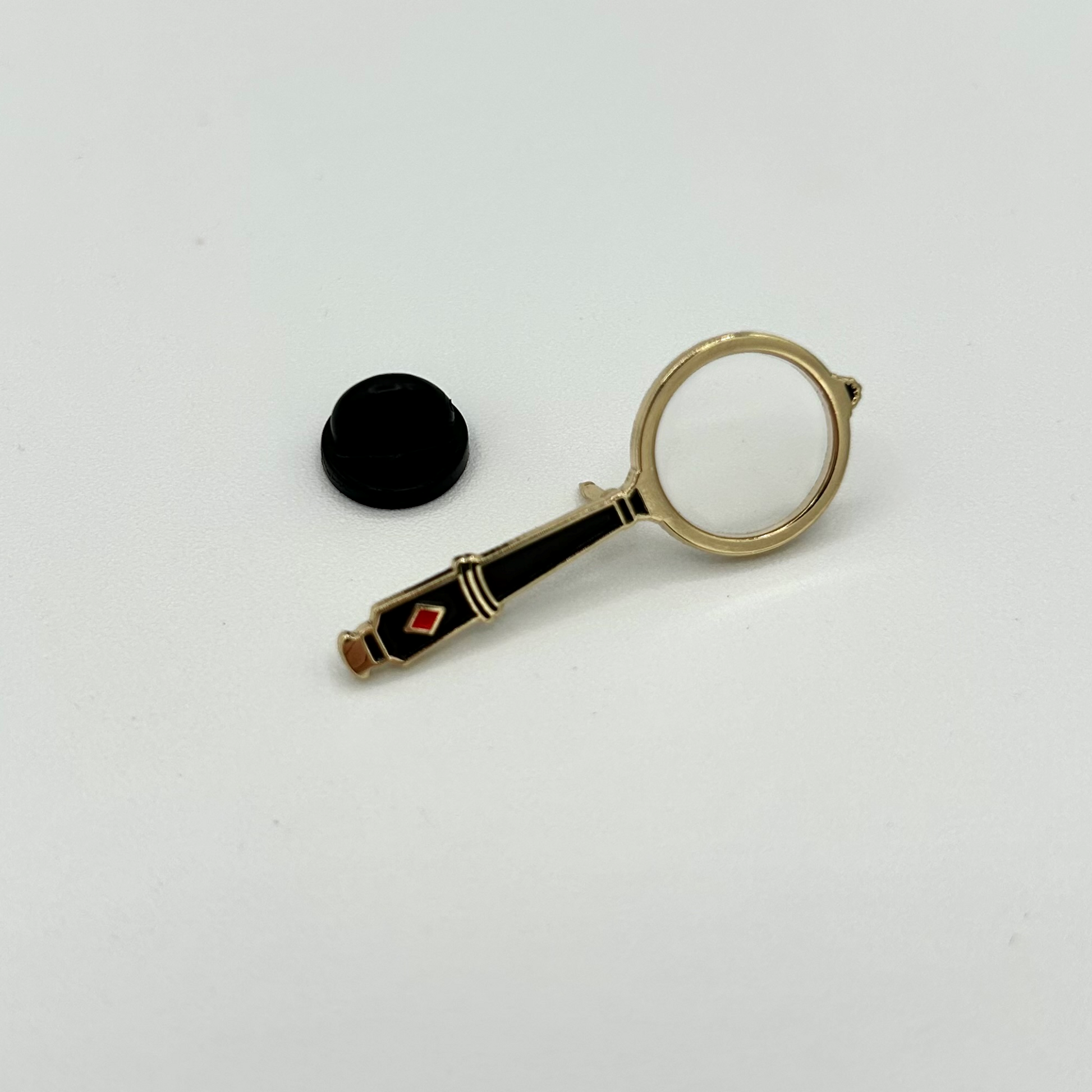 Decorative pin badge with a magnifying glass design on a white background.